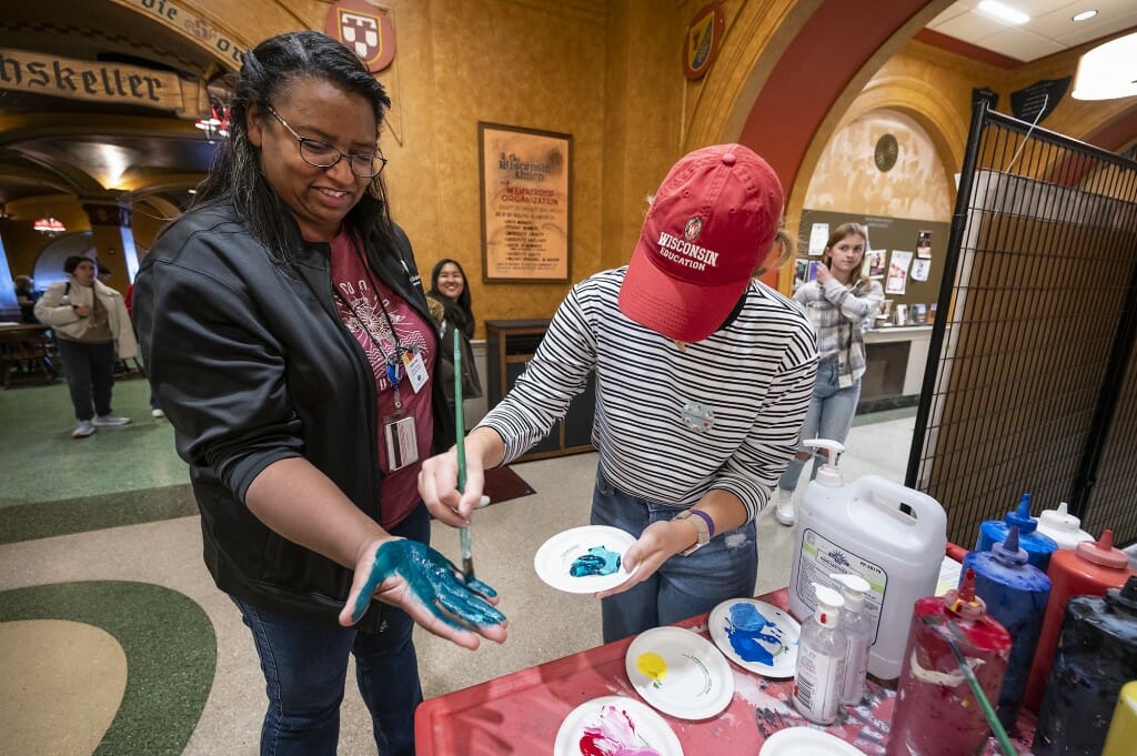 A person paints the hand of another person, which will be pressed onto the mural.