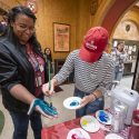 A person paints the hand of another person, which will be pressed onto the mural.