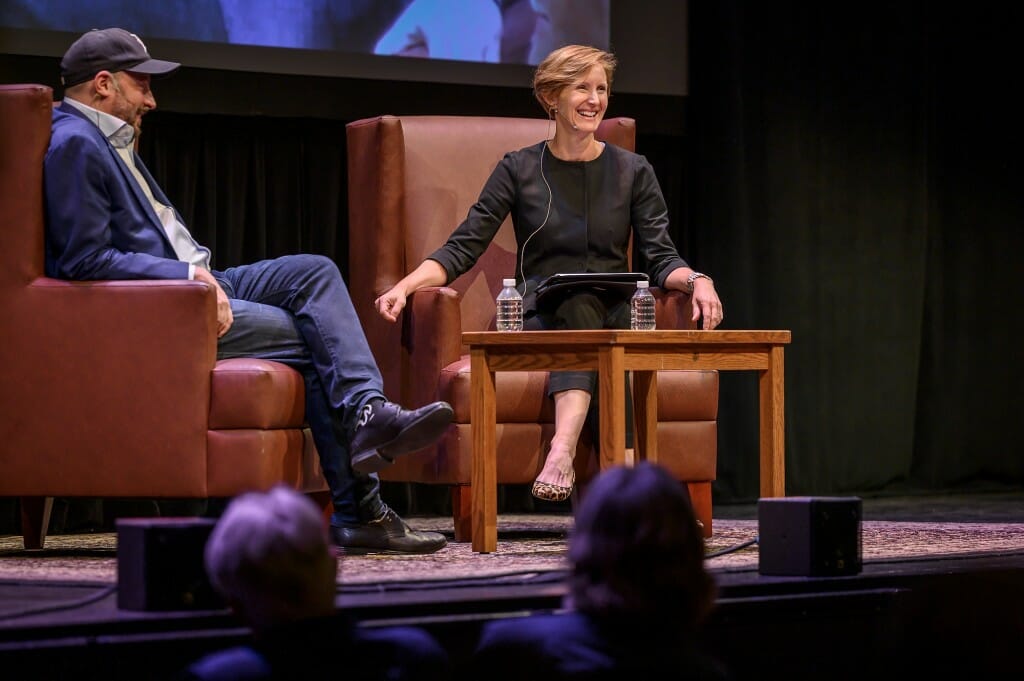 At right, Susan Webb Yackee smiles at the audience as she asks Nate Silver a question. They are seated in leather chairs on the stage in Shannon Hall.