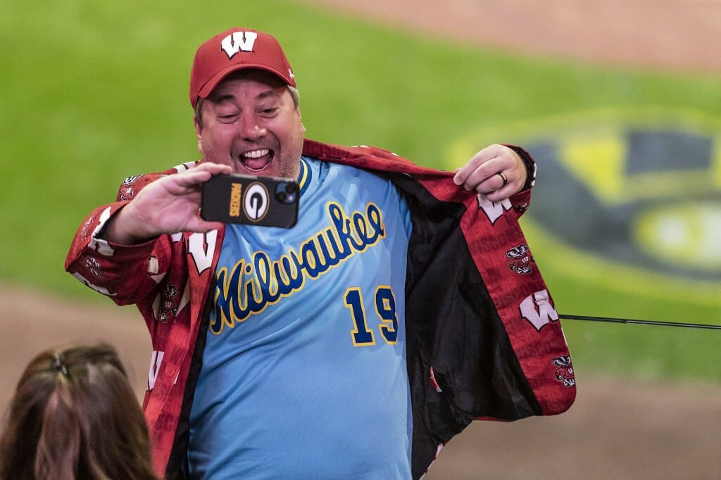 A man with multiple shirts smiles into his cell phone camera.