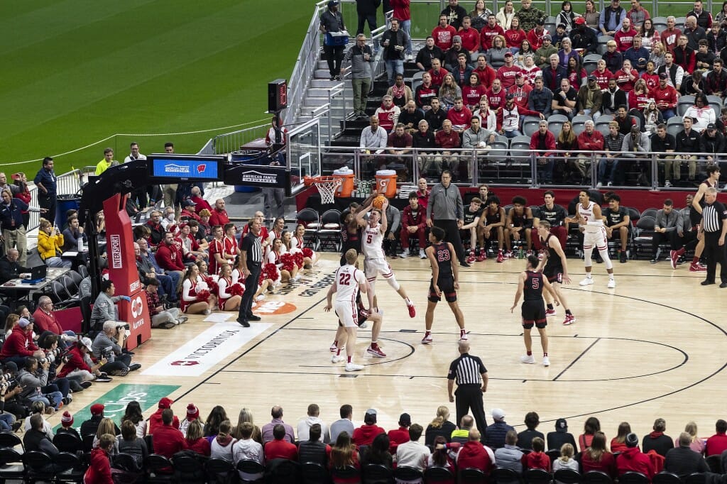 Men play basketball on a court set up on a grass baseball field.