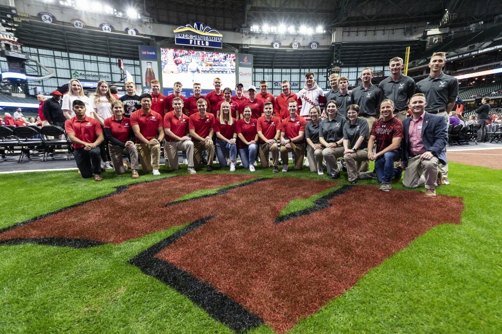 A group of people clad in red kneel on a grass surface and have their photo taken.