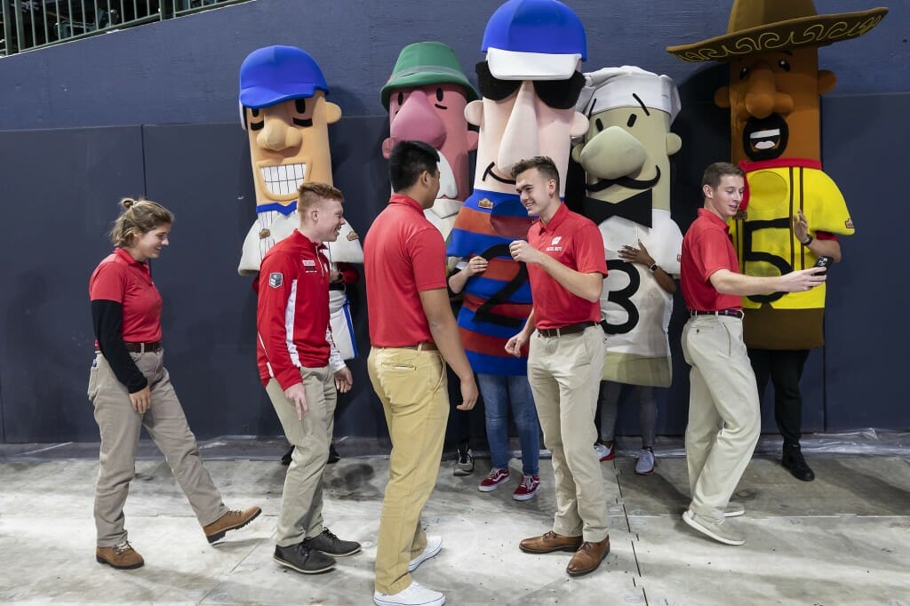 People clad in red shake hands with several people dressed up in sausage costumes.