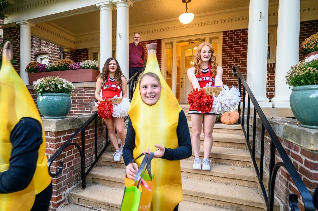 Two trick-or-treaters dressed as bananas smile as they leave Olin House with more candy. Two members of the Spirit Squad wave from the steps.