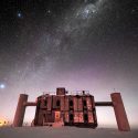 Front view of the IceCube Lab at twilight, with a starry sky showing a glimpse of the Milky Way overhead and sunlight lingering on the horizon.