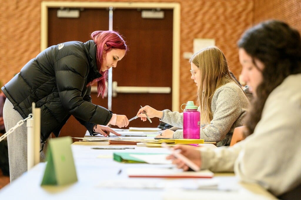 A student bends over a table and shows her ID to a poll worker.