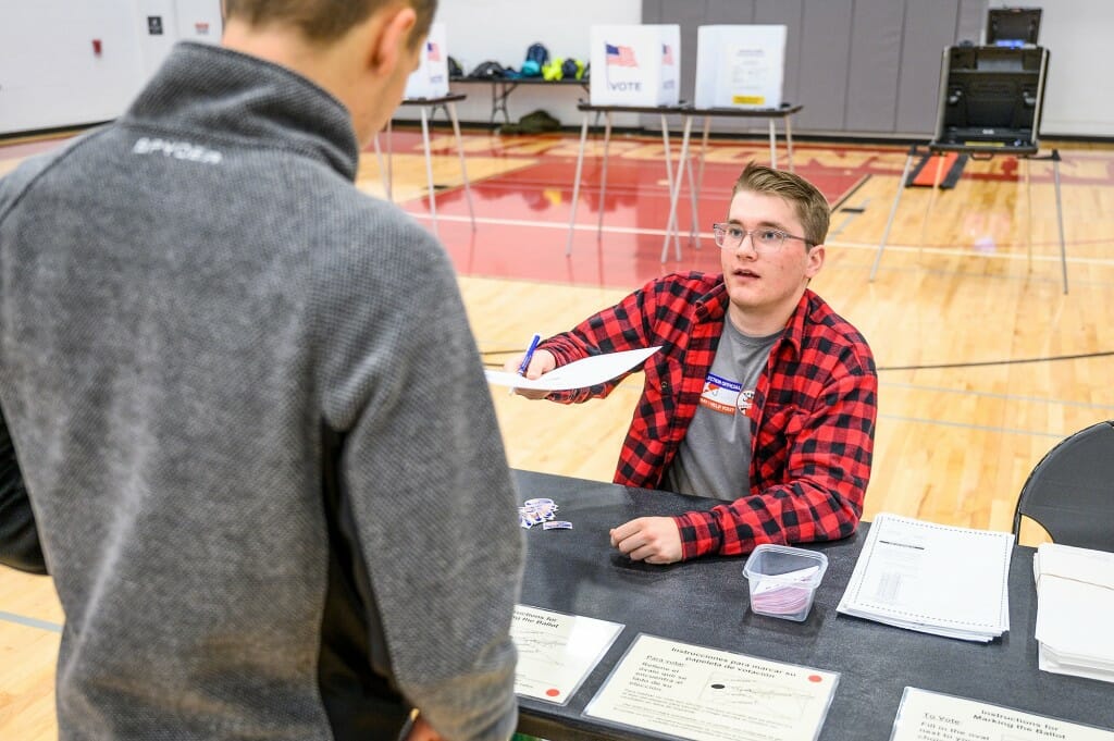 A seated poll worker hands a ballot to a voter.