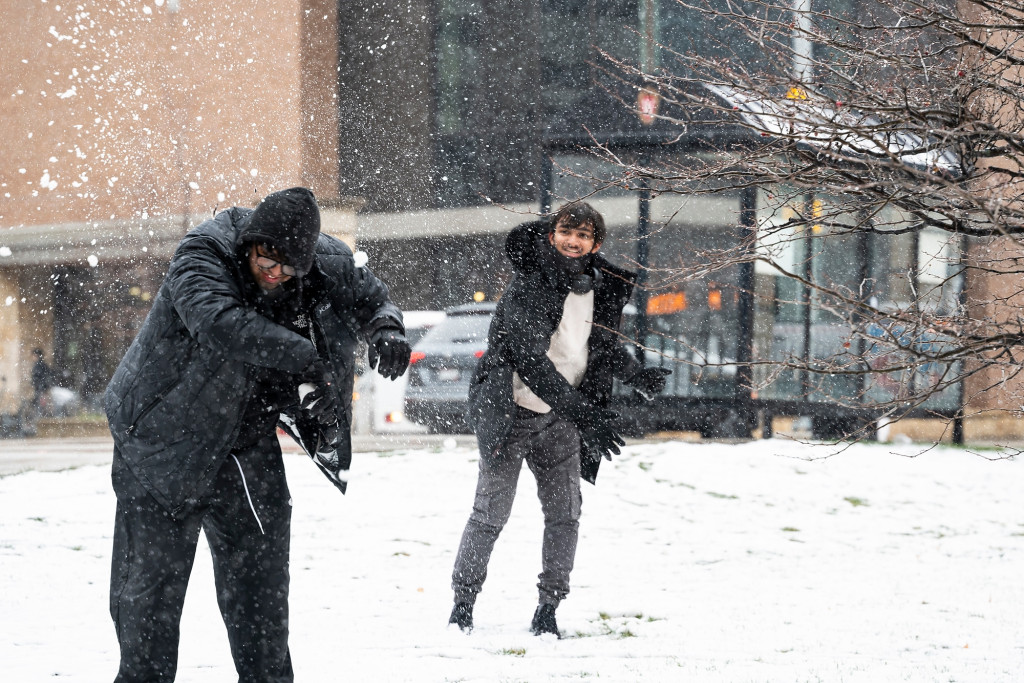 Two people throw snowballs at each other.