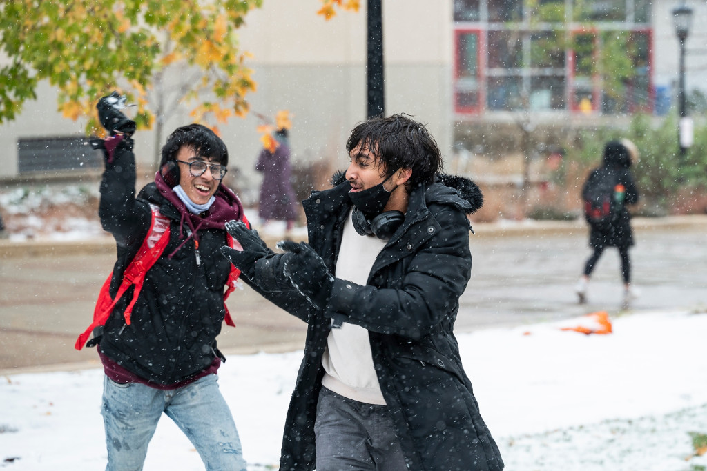 Two people throw snowballs at each other.