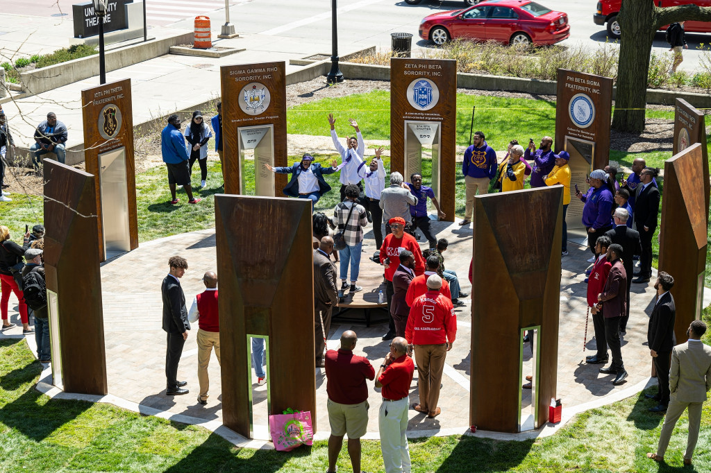 An aerial view of the new Divine Nine Garden Plaza with a crowd of visitors walking among a ring of nine historical markers.