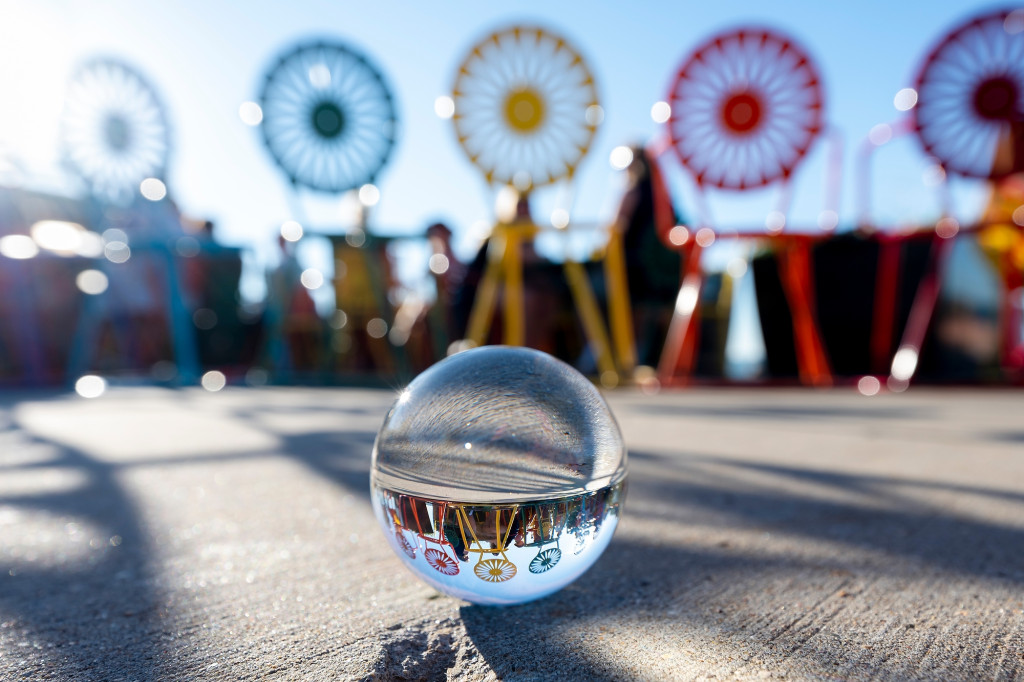 On a sunny day, a glass orb sitting on pavement reflects a row of rainbow Union Terrace chairs.