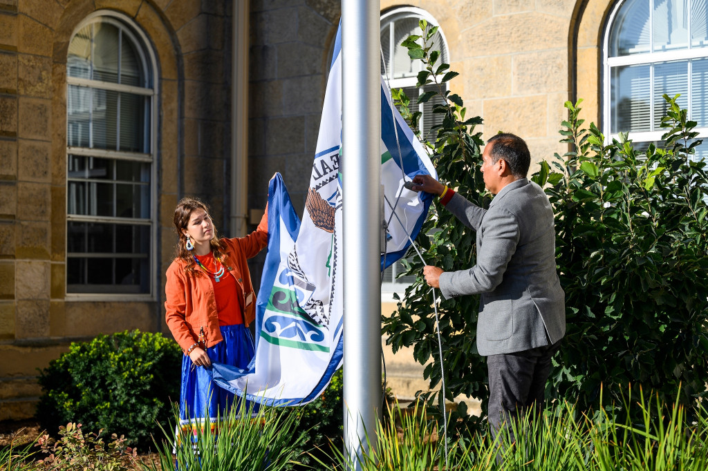 Sagen Quale and Aaron Bird Bear hold the ends of the flag of the Ho-Chunk Nation as they raise it up a flagpole at Bascom Hall on a warm and sunny fall day.