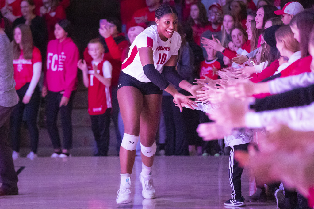 A uniformed volleyball player high fives a bunch of kids.