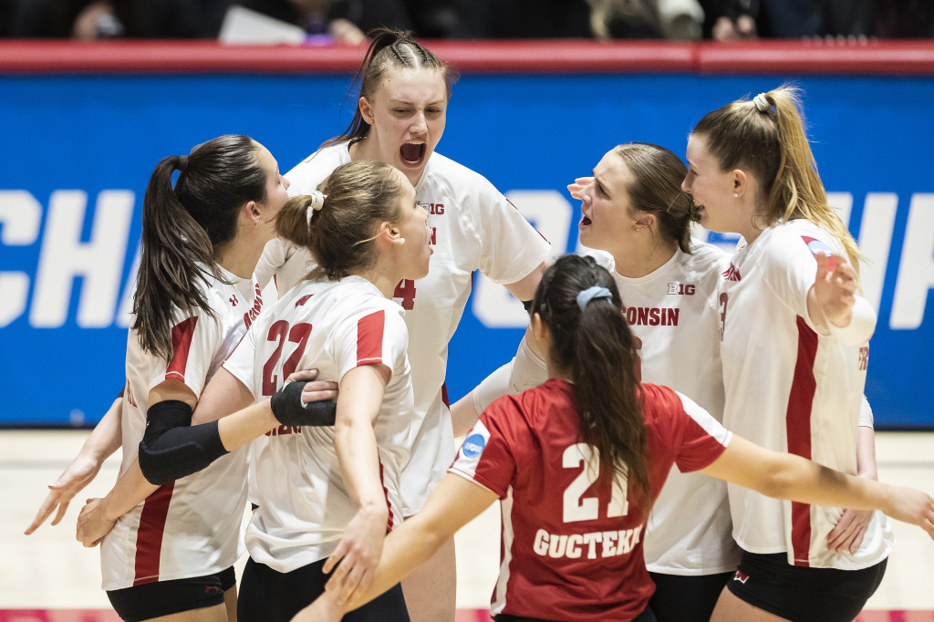 Volleyball players huddle up on the court, one of them shouting encouragement.