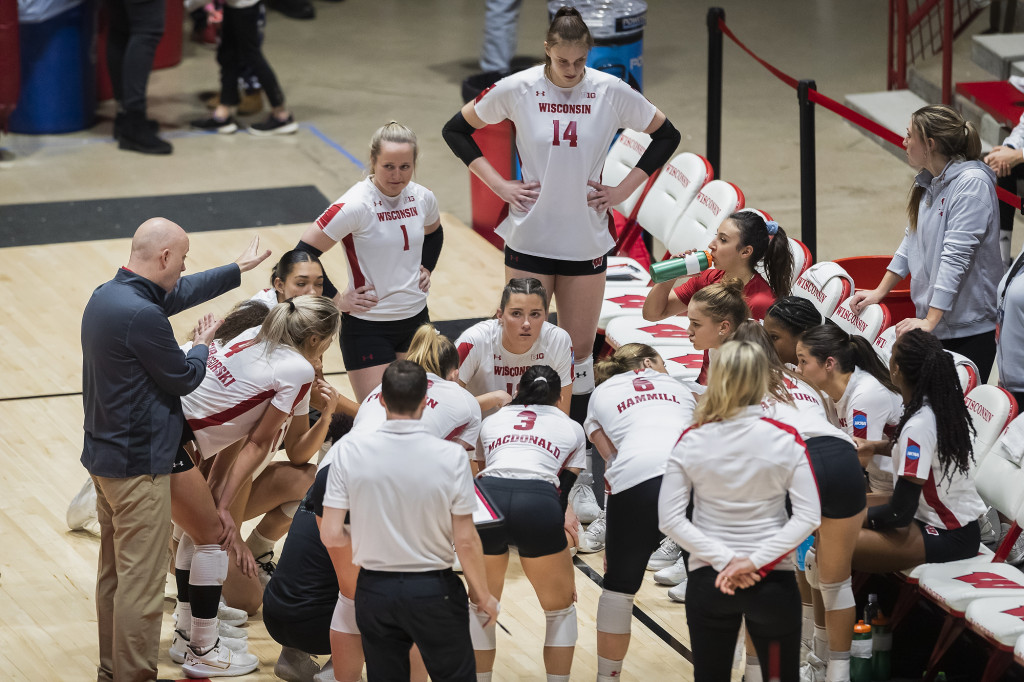 The volleyball team huddles and listens to the coach, who talks and gesticulates.