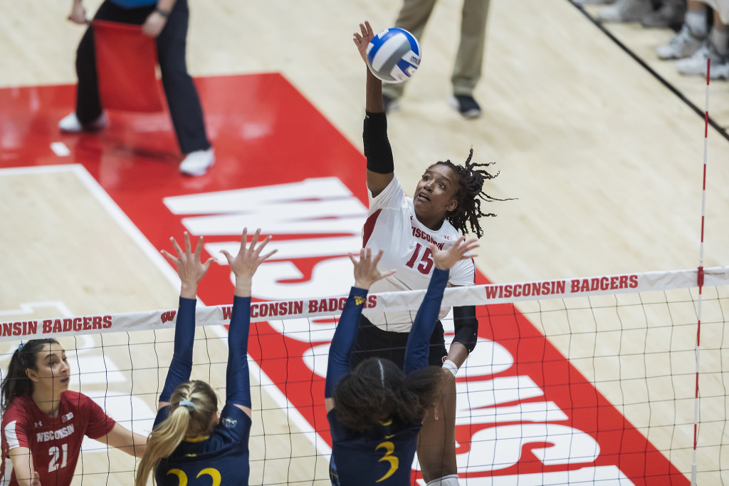 A volleyball player reaches up an arm to spike the ball just over the net.