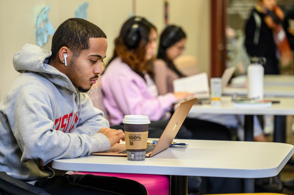 People sitting at desks in a row examine their books.