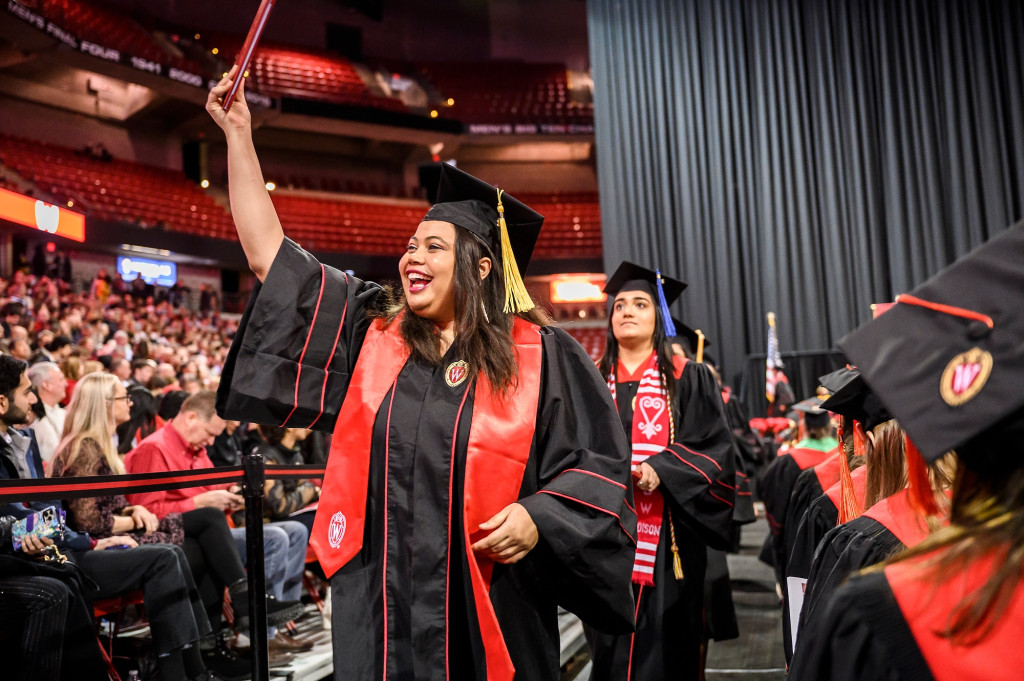 A woman holds up her diploma and shouts in glee.