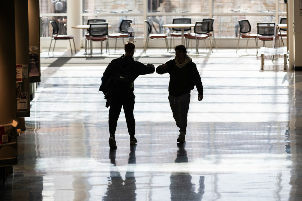 Two people shown in silhouette elbow bumping.