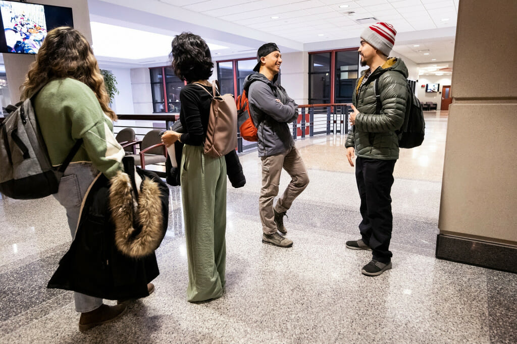 Two people talk amid a crowd of students in a hallway.