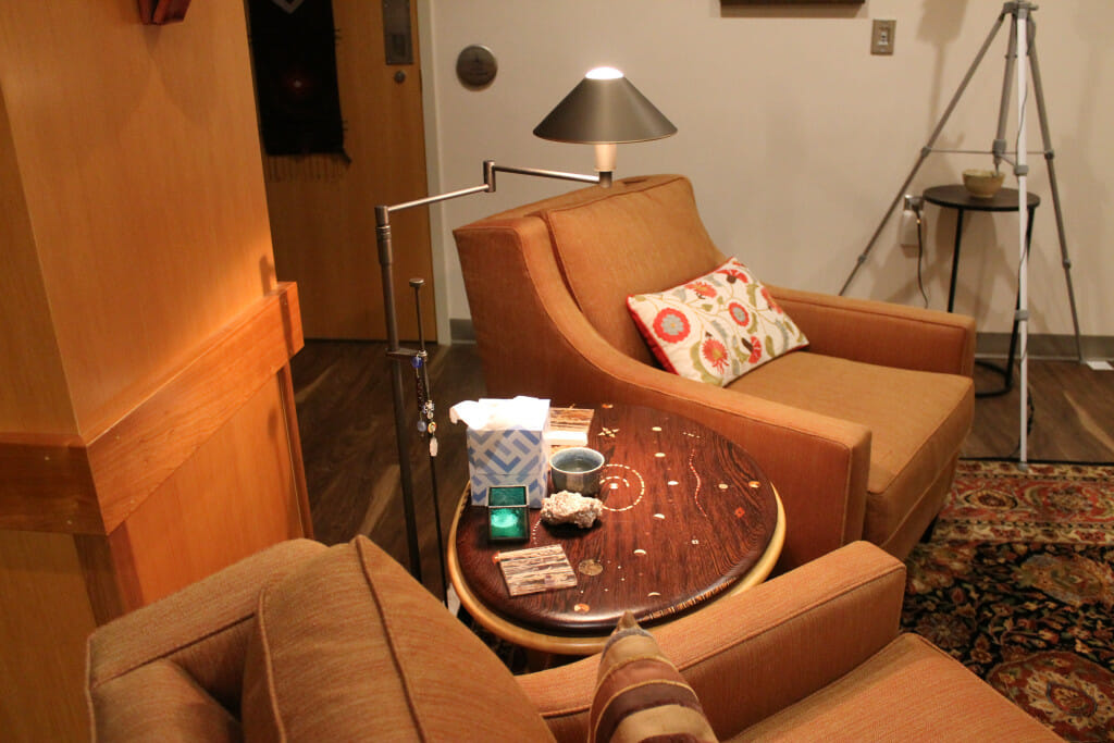 Another view of the psychedelic testing room shows two brown arm chairs with a round wooden end table in between. The space is decorated to resemble a living room.