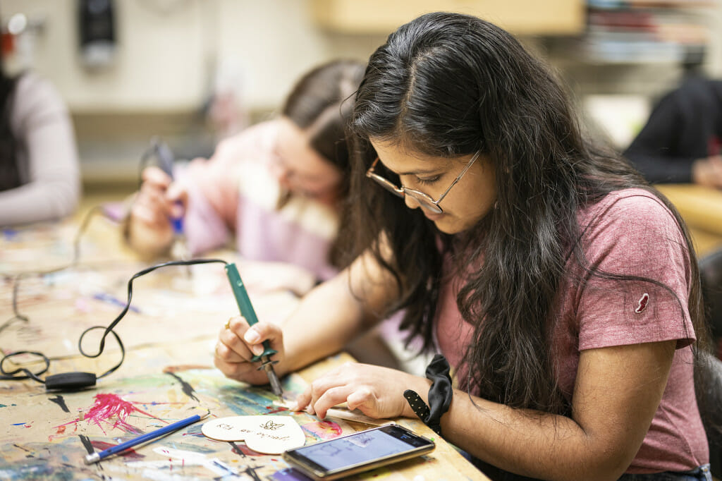 Undergraduate Anupreksha Jain uses a wood-burning iron to create Valentine's Day art.