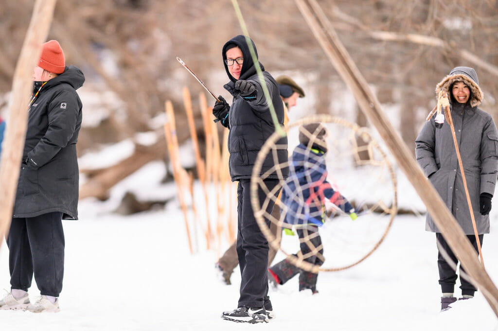 Undergraduate Kane Funmaker, Ho-Chunk Bear Clan member, prepares to throw a lance at a swinging hoop in the dakobijigan-minawaa zhiimaagan game while his partner, graduate student Shiqi Shen, looks on.