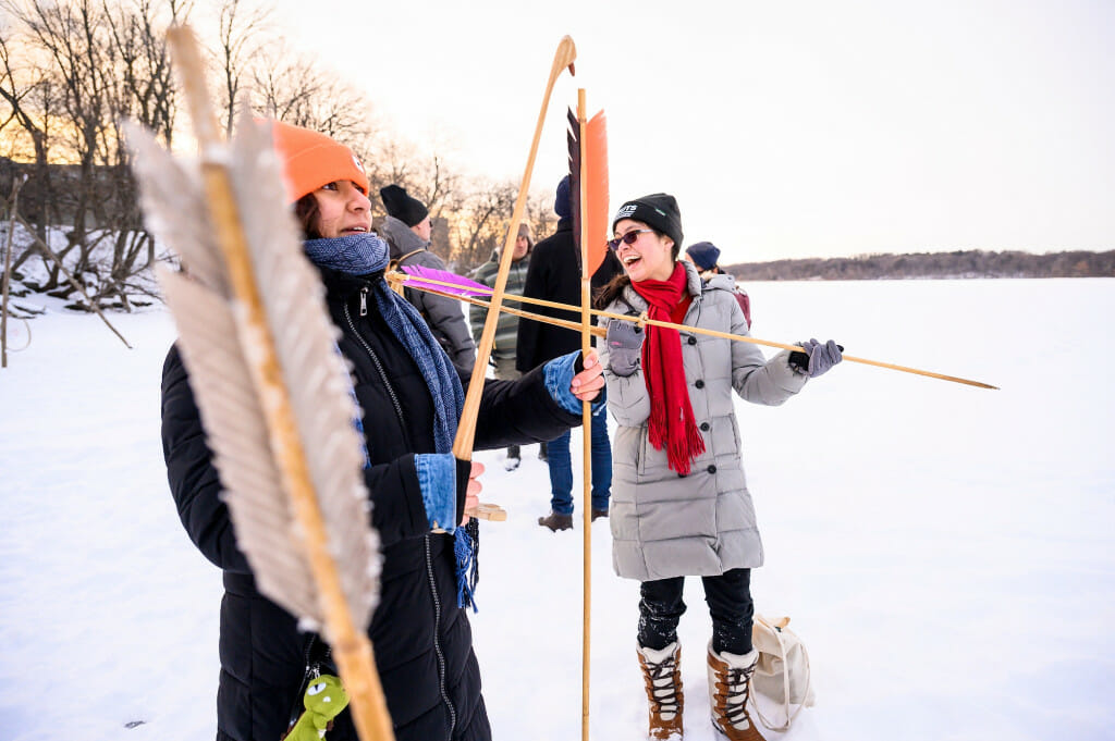 Undergraduate Isabella Escobar (of the Purépecha Nation), right, laughs while Diana Vera (of the Otomi Tribe) fits a spear onto an atlatl (spear throwing tool).