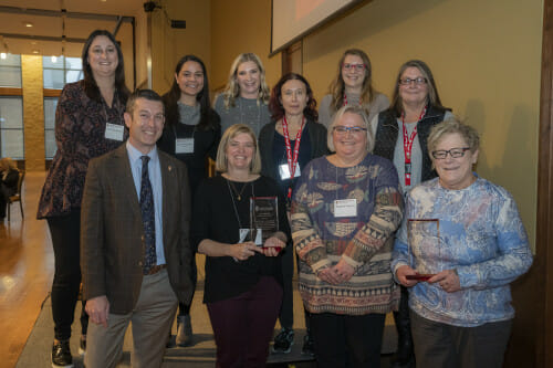 Pictured (L-R, front): Patrick Sheehan, Leanne Morris, Liz Valentine, Lynn Sullivan; (L-R, back): Erica Fini-Marten, Anna Vembu Julian, Lauren Bowers, Lili Gagliano, Anne Yorde, Marci Birkes. The group stands in two rows in a conference room setting. They are smiling to the camera.