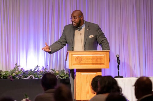 A man speaks at a podium, and gestures.