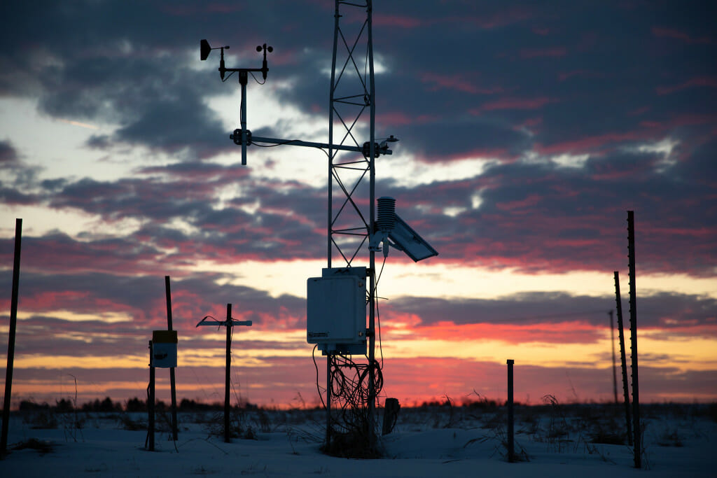 Some large pieces of equipment in a farm field are silhouetted by a sunset.