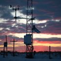 Some large pieces of equipment in a farm field are silhouetted by a sunset.