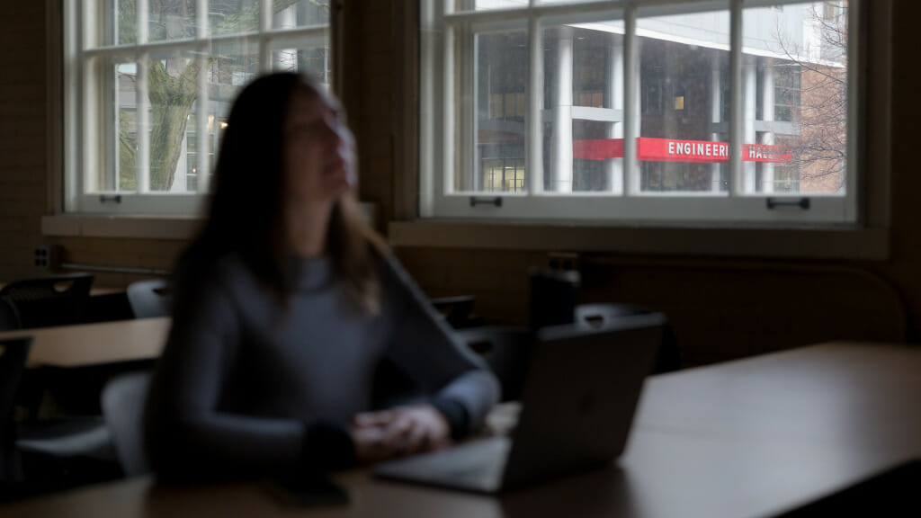 A female student sits at a desk, with the engineering building in the background.