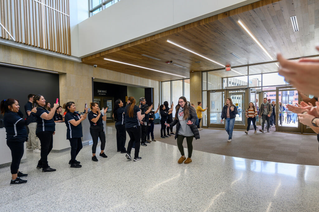 A student walks into the shiny exterior and is greeted by a group of people.