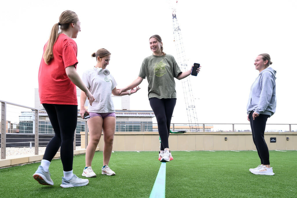 At center, Elise Vorpahl tries out a slackline with the help of Anna St. Martin while Alex Nonn (left) and Natalia Kwiecien (right) look on in the outdoor fitness area on the third floor.