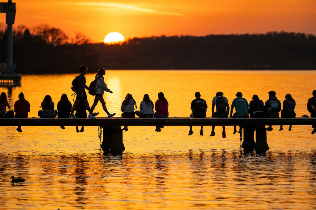 Coming out of winter hibernation, people line the Goodspeed Family Pier to chat in the warmth and watch a spring sunset fall over Lake Mendota and Picnic Point (on the horizon).