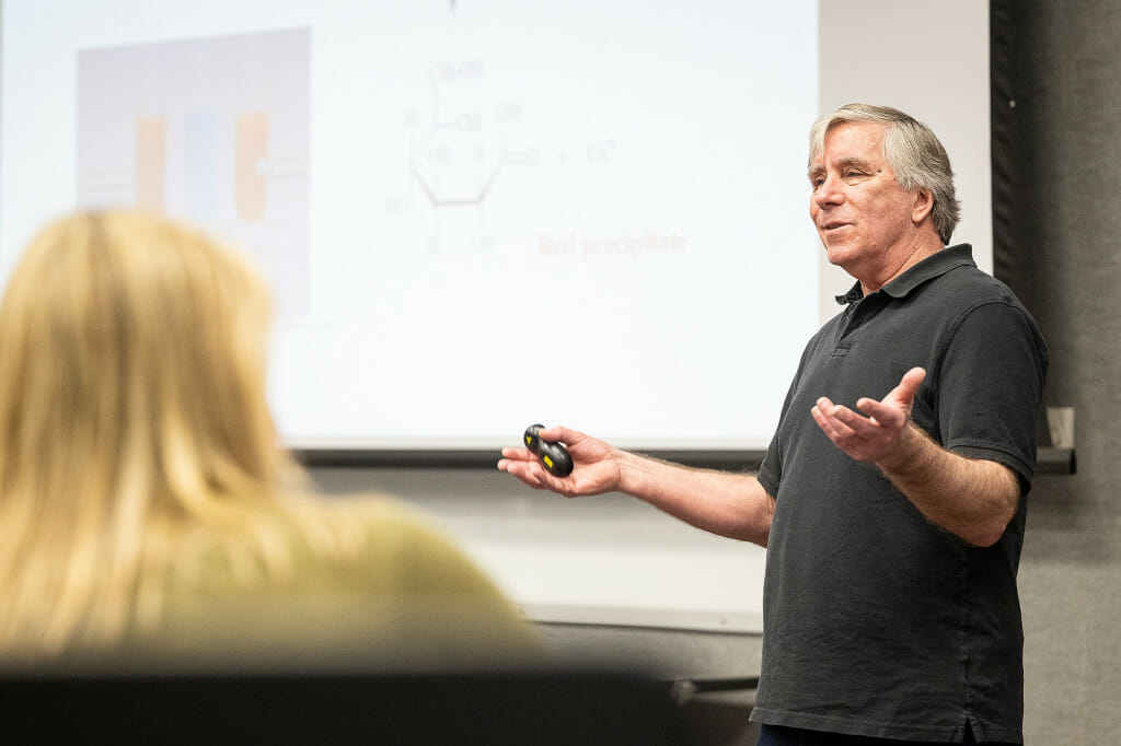 A man gestures while talking to a classroom.