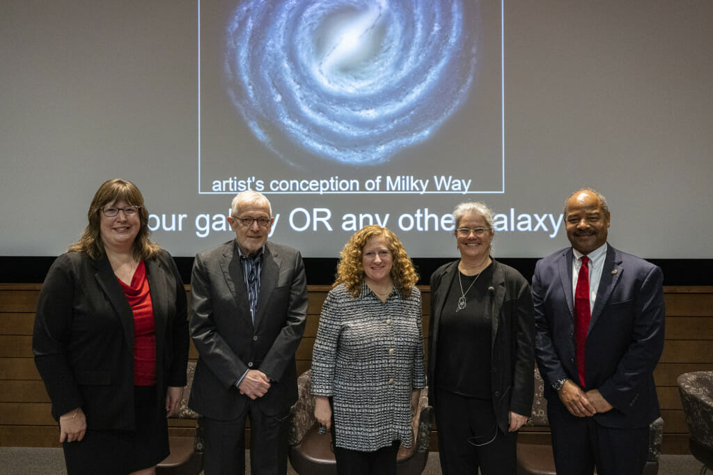 Five people stand in front of the stage and look at the camera.