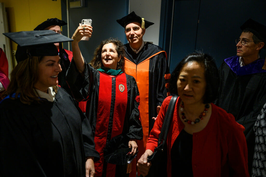 A woman holds up a cell phone to take a selfie of her and a man standing behind her. 