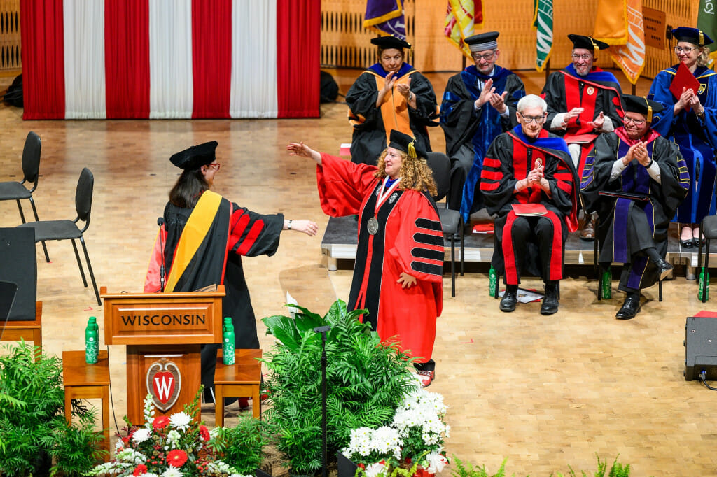 Raken Walsh croses the stage to embrace Chancellor Mnookin. They are both wearing academic robes and hats.