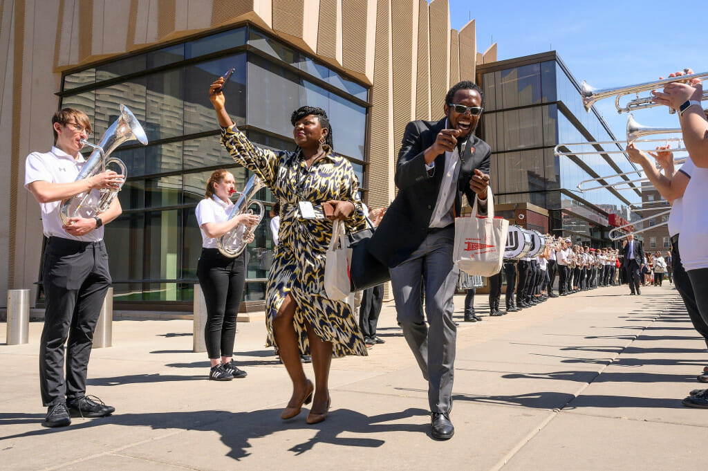 Two people wave to the musicians lining the sidewalk.