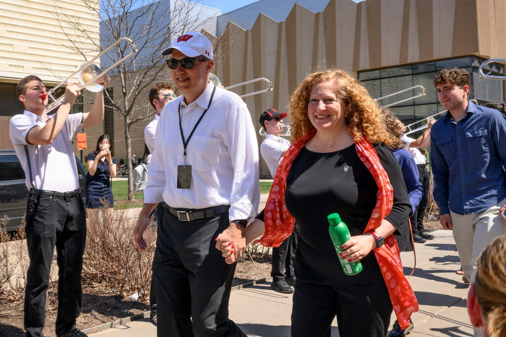 A couple hold hands as they walk down the sidewalk.