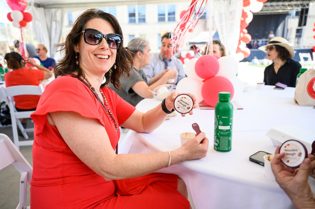 A woman sits at a table, tasting her ice cream from a cup.