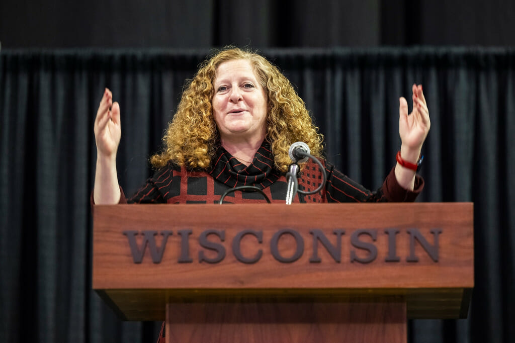 Chancellor Jennifer Mnookin stands behind a podium with her hands raised as she speaks to an audience off camera.