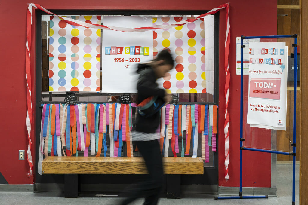 A person blurred in motion walks by a sign that marks the Shell's years: 1954 to 2023.