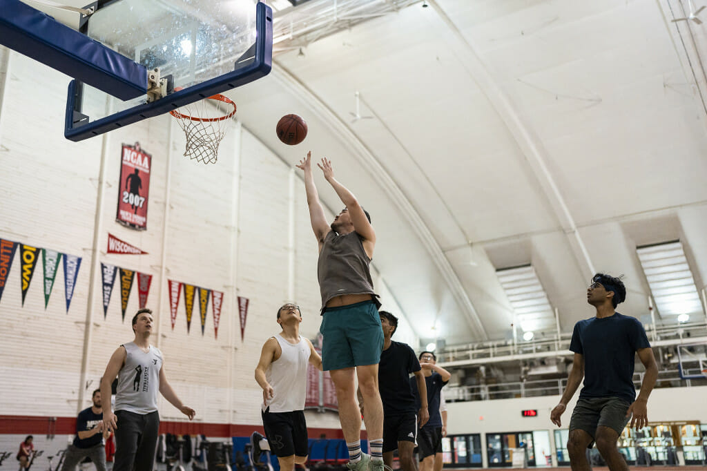 A person shoots a basketball on the Shell basketball court, as other players react.