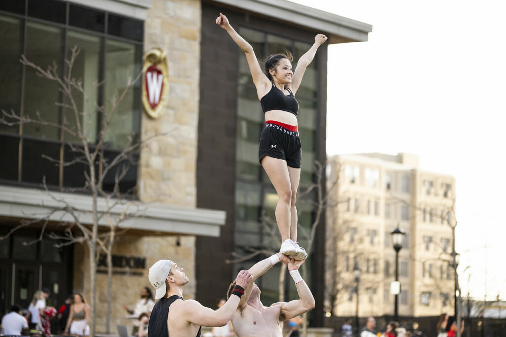 Two men hold a woman in the air by her feet - she raises her arms.