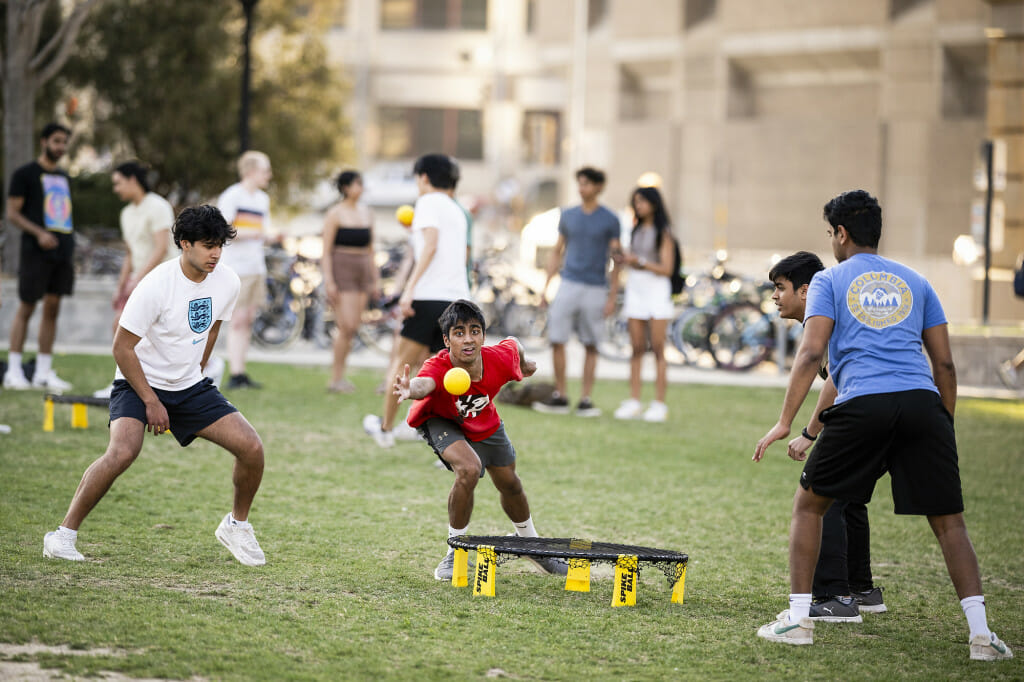 Students stand around a small trampoline that's the center of the spikeball game.