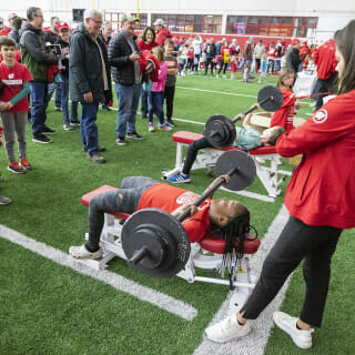 Young kids lay on their backs on a bench and try to bench press a barbell with weights.