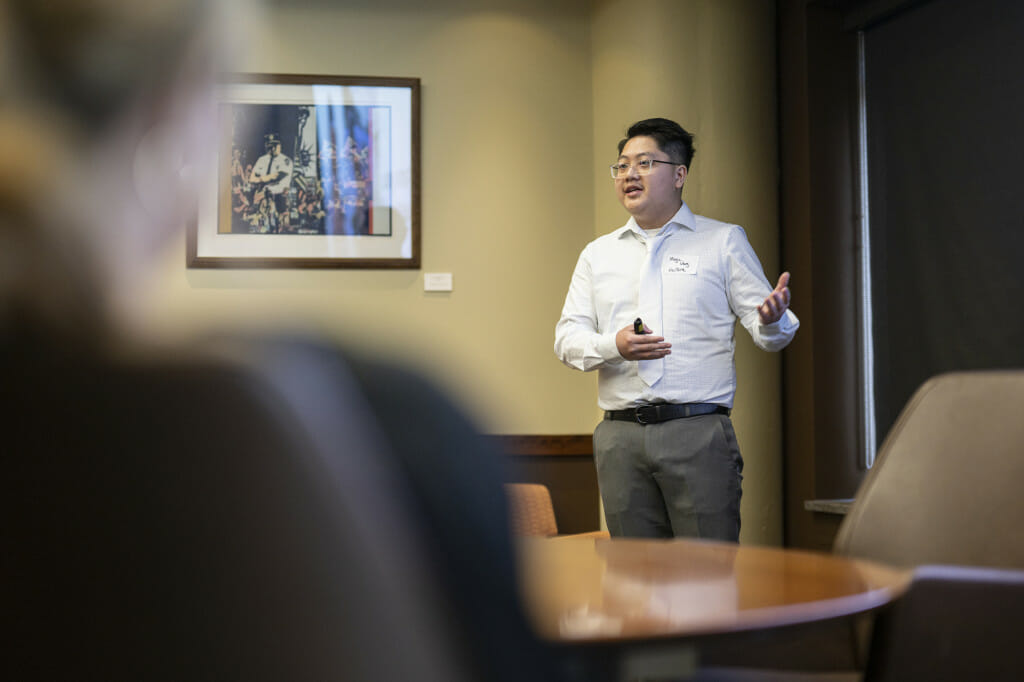 A man gesticulates as he talks in front of a crowd.